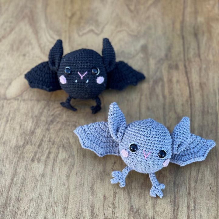 A black crochet bat and a light blue crochet bat on a wooden table